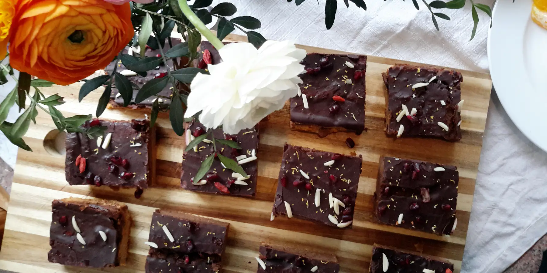 12 geschnitte Stück zuckerfreie Süßkartoffel Brownies liegen auf einem Schneidebrett unter einer weißen Blume.
