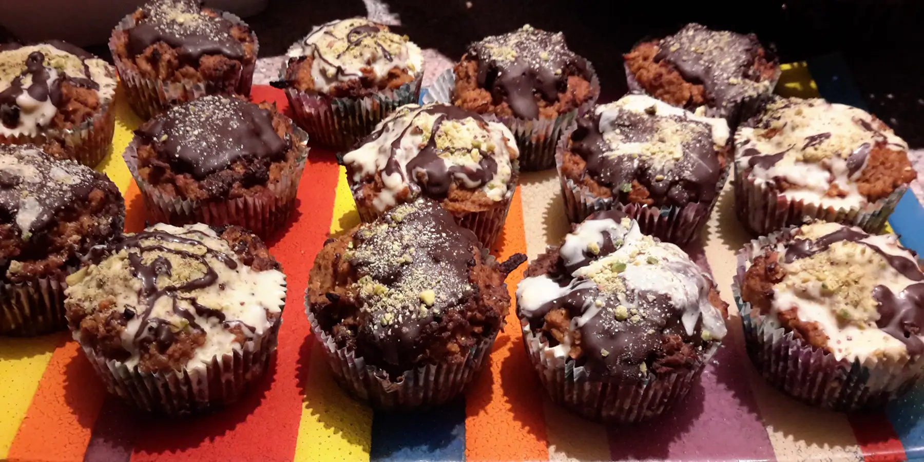 Leckere und gesunde Karotten Schoko Muffins in roten und bunten Förmchen auf einem Tisch, verziehrt mit weißer und dunkler Schokolade.