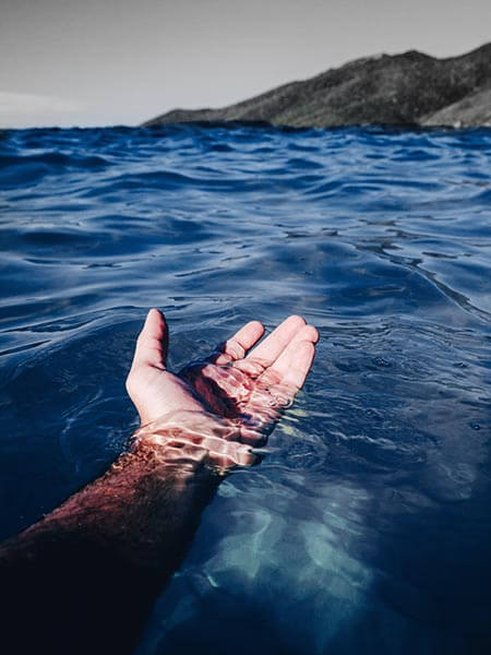 Eine Hand, ausgestreckt im blauen Wasser, im Hintergrund die Küste als Symbolbild für das Forum Mut.