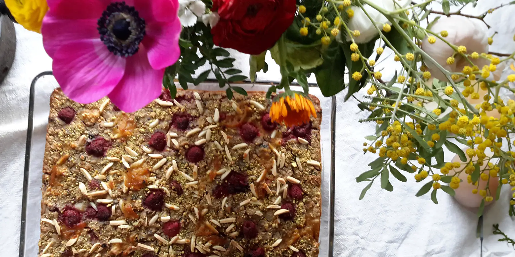 Eine Schüssel Himbeer-Haferporridge unter einem Strauß Blumen auf einem Tisch.