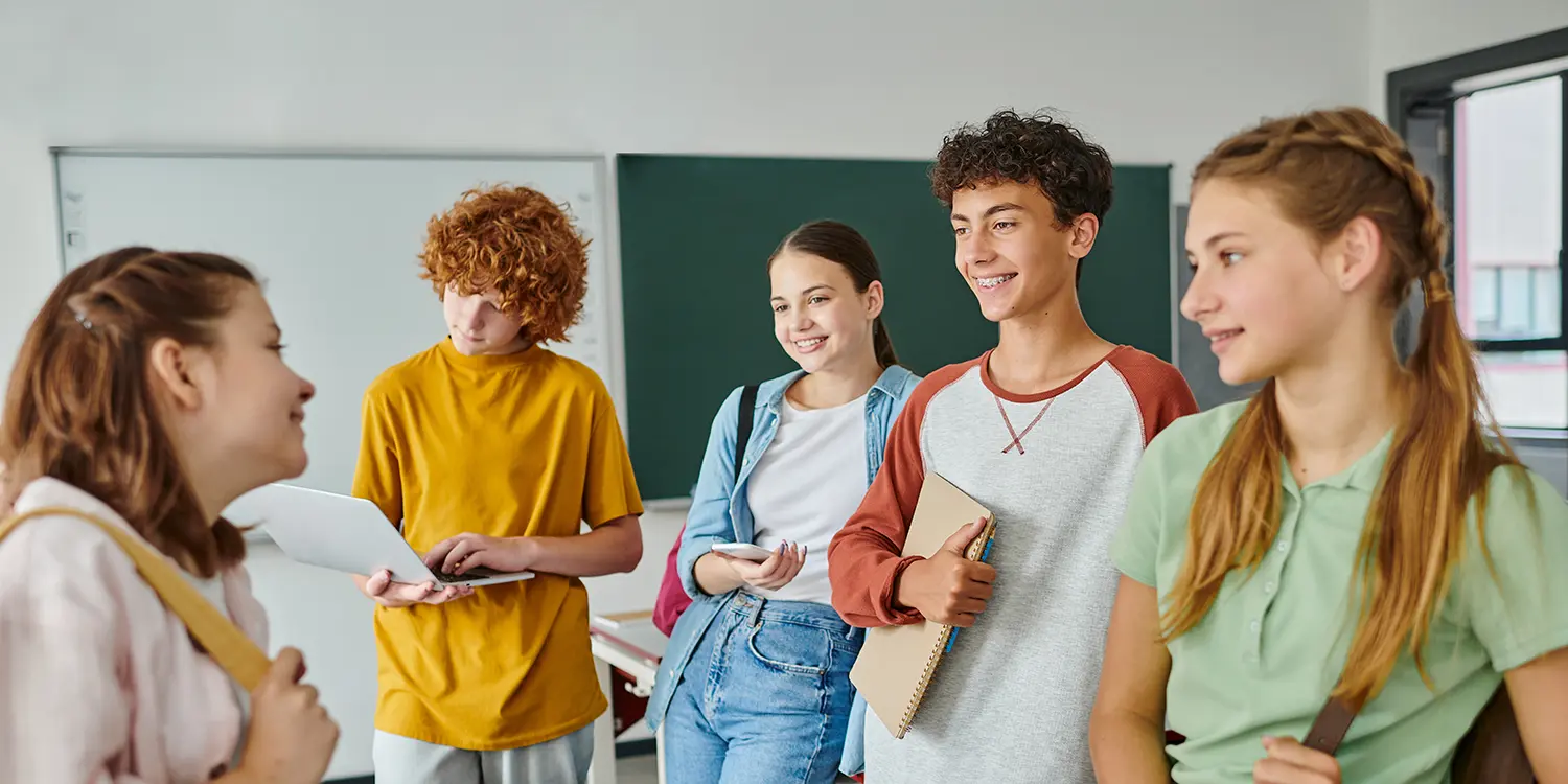 Gruppe von fünf Jugendlichen steht in einem Klassenzimmer zusammen als Symbol für den MHFA Ersthelfer-Kurs Youth.