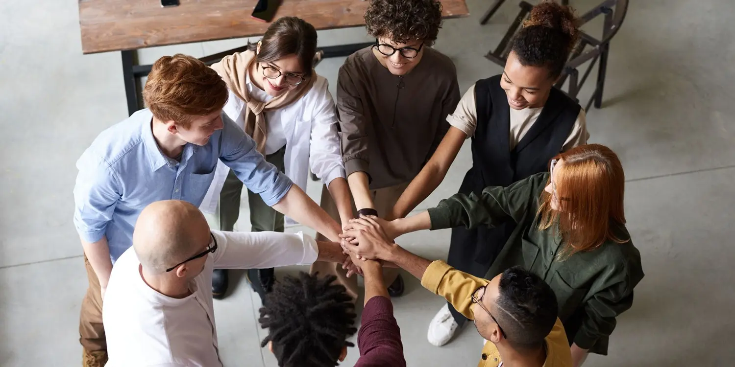 Ein Team aus acht Personen steht zusammen im Kreis und streckt jeweils eine Hand in die Mitte als Symbol für den gelernten Zusammenhalt bei MHFA Ersthelfer-Kurse für mentale Gesundheit in Unternehmen.
