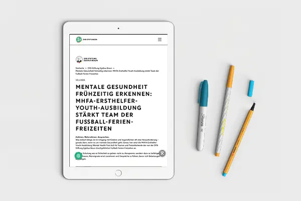 Mockup des Artikels "Mentale Gesundheit frühzeitig erkennen: MHFA-Ersthelfer-Youth-Ausbildung stärkt Team der Fußball-Ferien-Freizeiten" auf der Website der Stiftung des DFB (Deutscher Fußball-Bund).