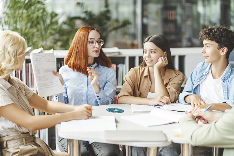 Eine Gruppe an Teenagern sitzen im Austausch mit ihrer Vertrauensperson an einem Tisch als Symbol für den MHFA Ersthelfer-Kurs Teen.